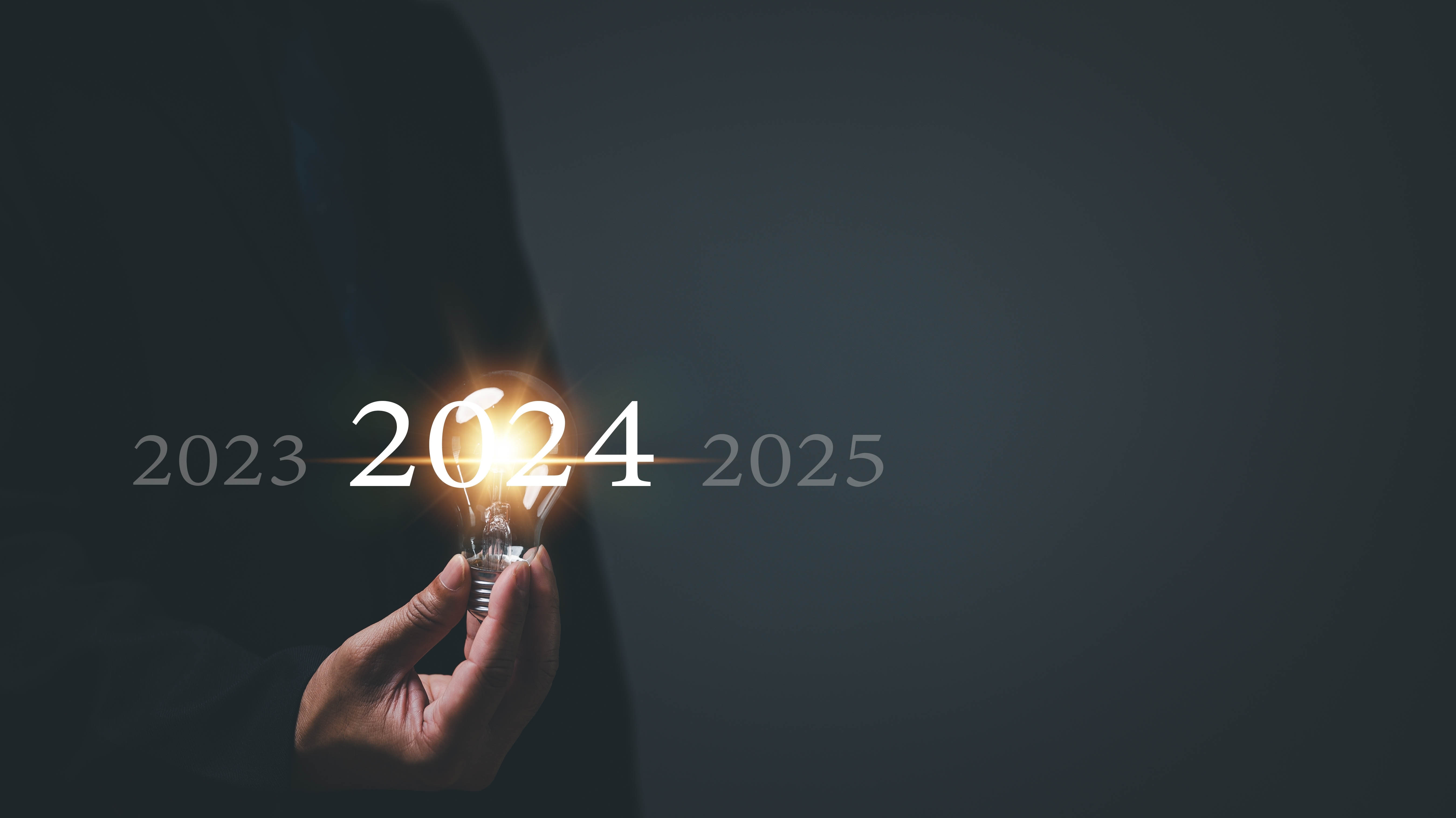 Close-up of a hand holding up a lit lightbulb directly over the numbers 2024
